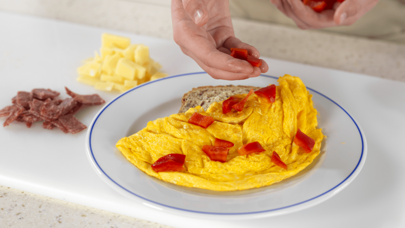 Legg de små bitene av paprika, salami og ost oppå omeletten.