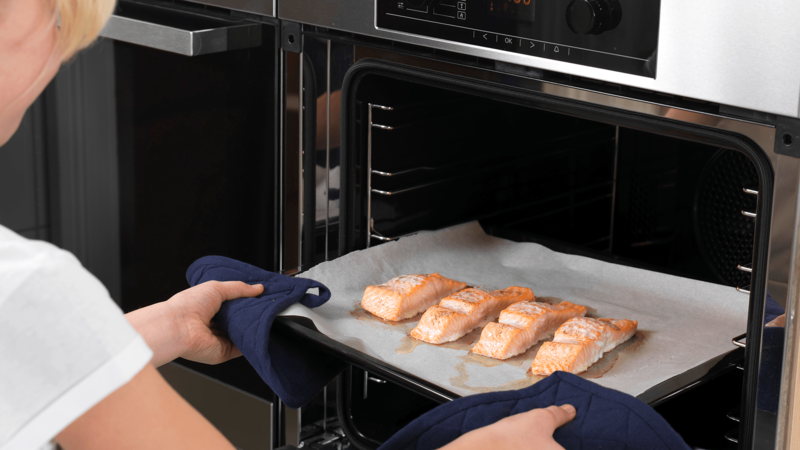Finn frem et gryteunderlag eller noe du kan sette det varme stekebrettet på. Bruk grytekluter og pass på slik at du ikke brenner deg når du tar laksen ut av ovnen.