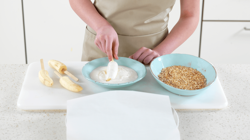 Sett frem en tallerken med bakepapir i nærheten. Start med å dyppe en bananbit i yoghurt.