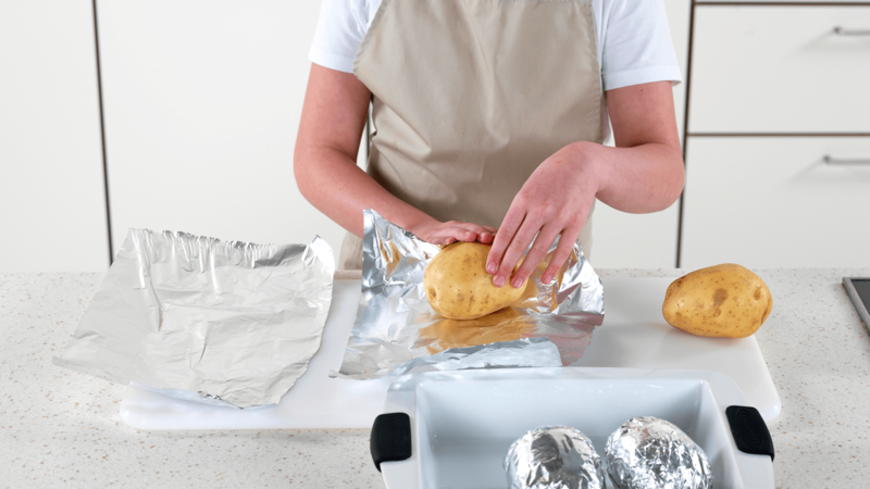 Vask og tørk potetene. Pakk dem inn i aluminiumsfolie og legg dem i en ildfast form.